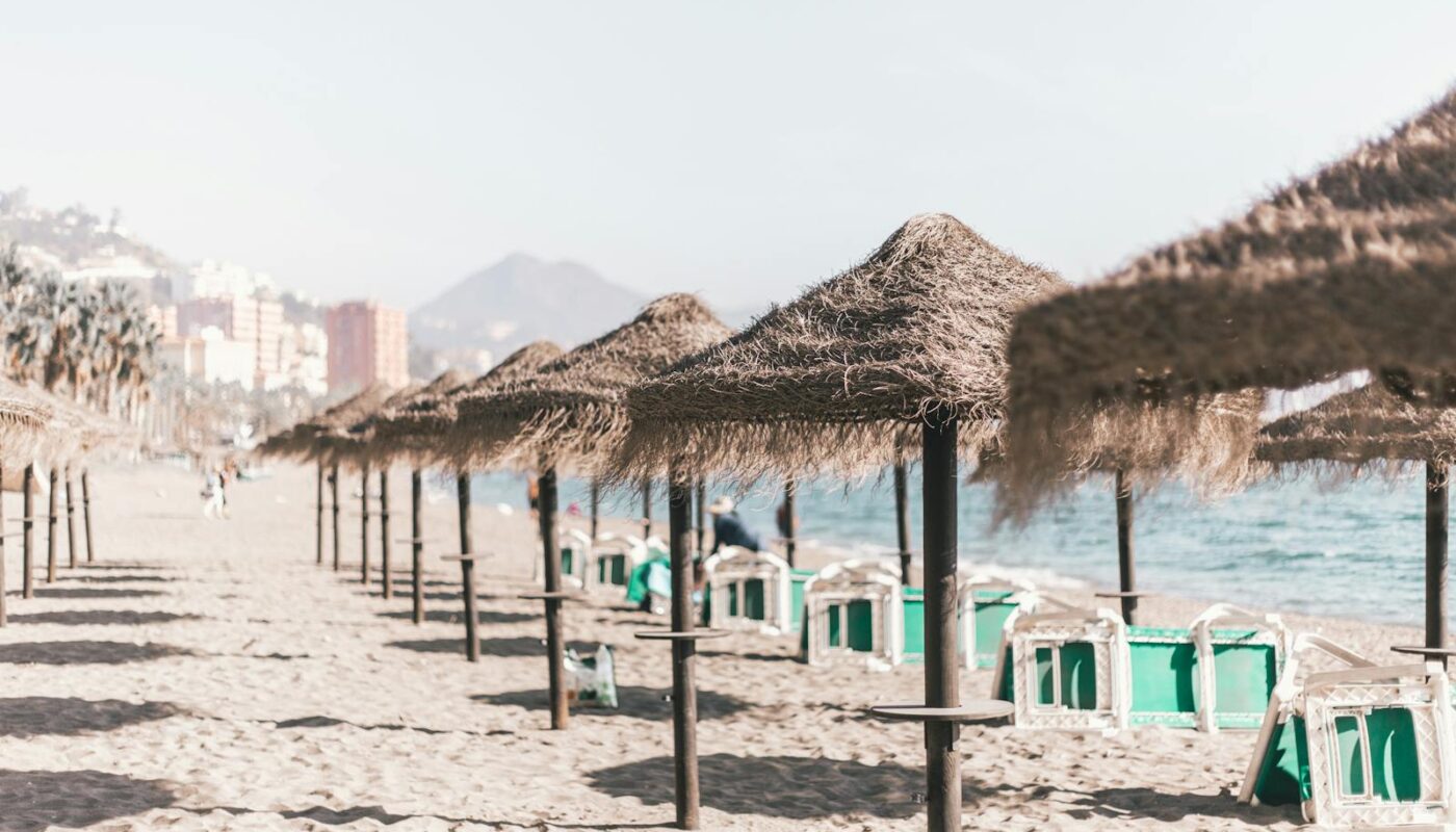A serene sandy beach with straw umbrellas and clear skies, perfect for a summer vacation in Malaga, Spain.