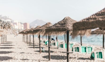 A serene sandy beach with straw umbrellas and clear skies, perfect for a summer vacation in Malaga, Spain.